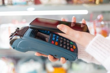 Bir kadının elleri ödeme terminalini tutuyor ve akıllı telefon kullanarak satın almaya para ödüyor. Boşluk ve kenar görüntüsünü kopyala. NFC, iş ve bankacılık işlemleri kavramı.