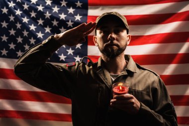 Anma günü. Üniformalı bir asker elinde mumla Amerikan bayrağının arka planına selam veriyor. Amerikan ulusal bayramı ve vatanseverliği kavramı..