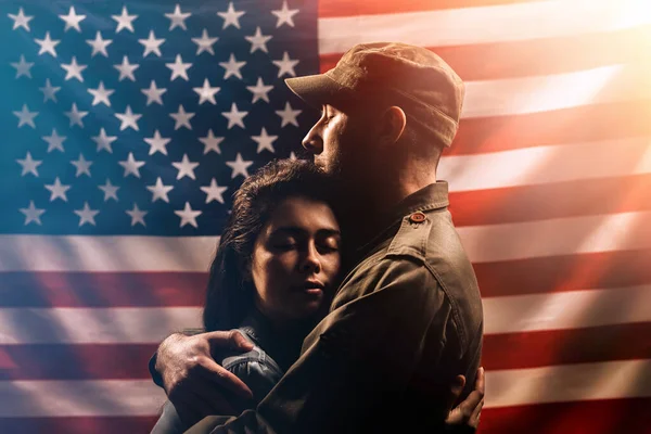Veterans Day, Memorial Day. A soldier embraces his woman. Couple on the background of the American flag. The concept of the American national holidays and patriotism