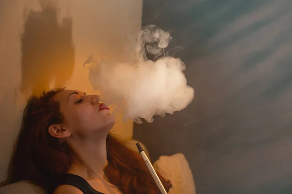 ソファの上でリラックス 美しい女性はフックを吸うと蒸気の雲を出す オレンジ — ストック写真