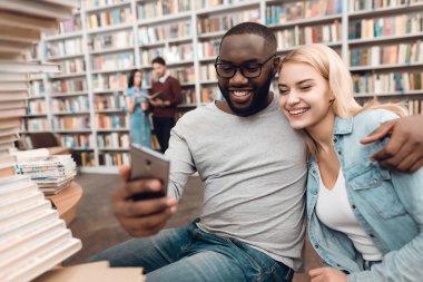 Etnik Afrikalı-Amerikalı adam ve Smartphone'da Kütüphane ve alma selfie masada oturan beyaz kız