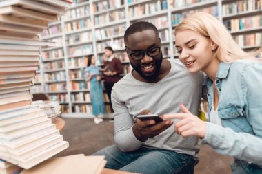 Etnik Afrikalı-Amerikalı adam ve Smartphone'da Kütüphane ve alma selfie masada oturan beyaz kız