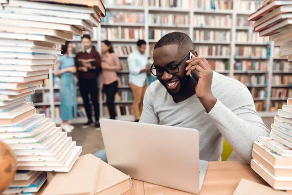 Ethnic African American Guy Sitting Library Using Laptop Talking Smartphone — Stock Photo, Image