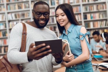 Siyah adam ve asial kız tablet kullanarak Kütüphane, masada oturan etnik çok kültürlü öğrenci grubu
