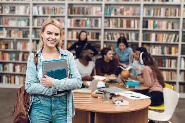 Kütüphane, masada oturan beyaz kız defter ile ayakta etnik çok kültürlü öğrenci grubu
