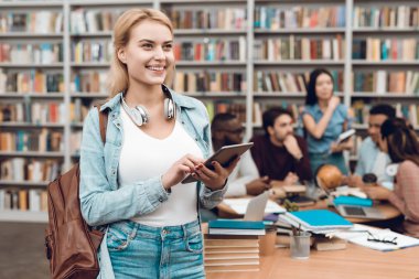 Beyaz kız tablet kullanarak tablo Kütüphanesi'nde oturan içinde etnik çok kültürlü öğrenci grubu