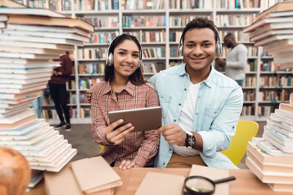 Ethnic indian mixed race girl and guy sitting in library and using tablet