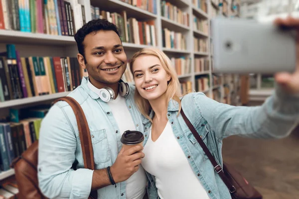 Ethnic indian mixed race guy and white girl in library and taking selfie on smartphone