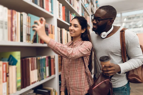 Ethnic indian mixed race girl and black guy surrounded by books in library and looking for books