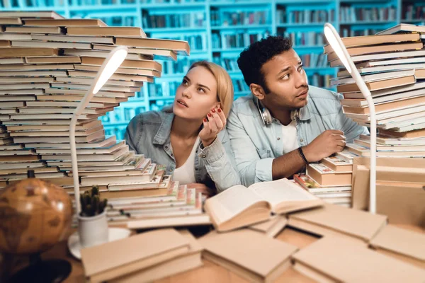 Ethnic indian mixed race guy and white girl sitting at table surrounded by books in library