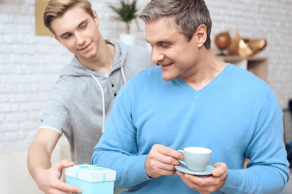 Father drinking coffee while son surprising him with birthday present