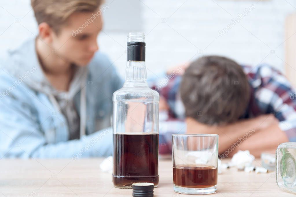 Drunk father lying on table with glass and bottles while son trying stop him