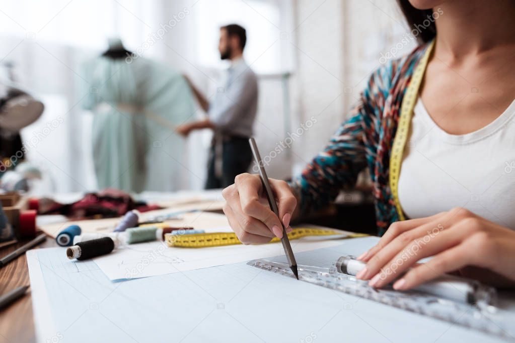 female designer making sketch while man working on mannequin in tailor shop 