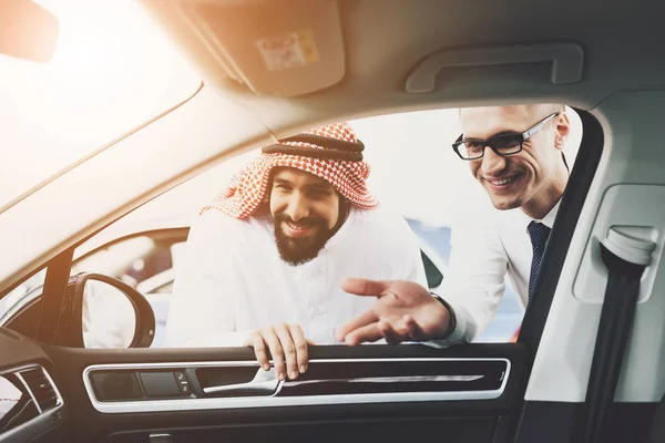 salesman help choosing new auto to Arabic man in thawb at car dealership