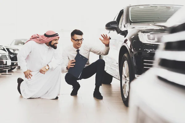salesman help choosing new auto to Arabic man in thawb at car dealership
