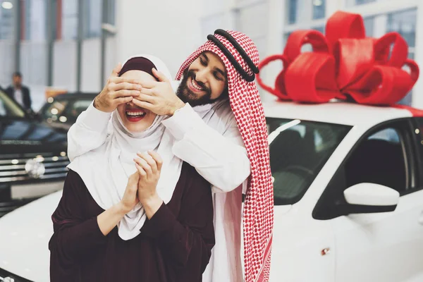 Arabic couple at car dealership, man presenting new car his wife