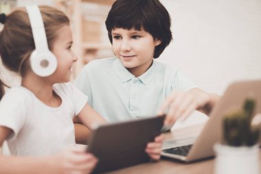 Tablet ve dizüstü bilgisayar ile masada oturan kardeş