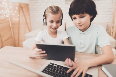 Tablet ve dizüstü bilgisayar ile masada oturan kardeş