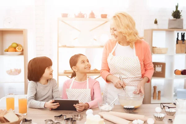 grandmother cooking at kitchen while grandchildren using tablet