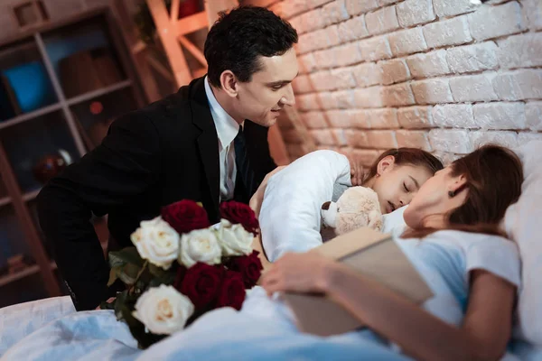 man with roses bouquet putting to bed small daughter while mother sleeping with book