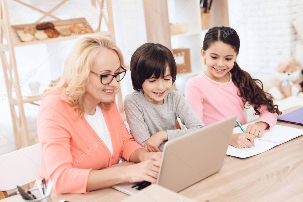 Grandmother with laptop helping grandchildren making lessons  