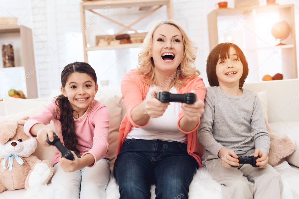 grandmother sitting on couch and playing video games with grandchildren  