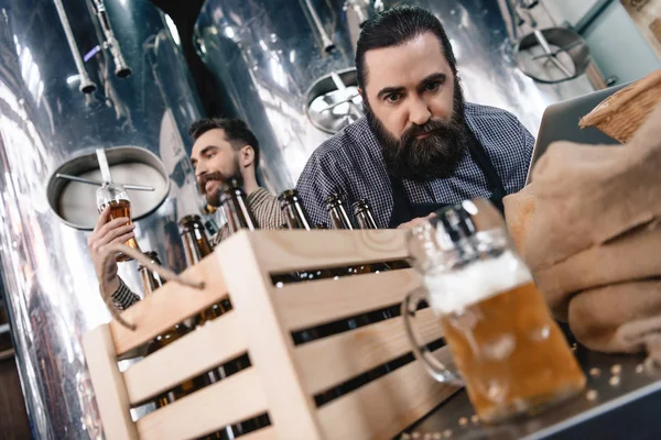 Concentrated man watching at beer mug while another man looking at density of beer