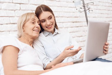 Yatakta yaşlı kadın bakmakta ve dizüstü bilgisayar kullanarak bir kız