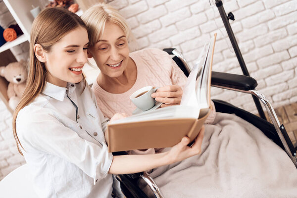 Girl nursing elderly woman, they looking pictures in photo album