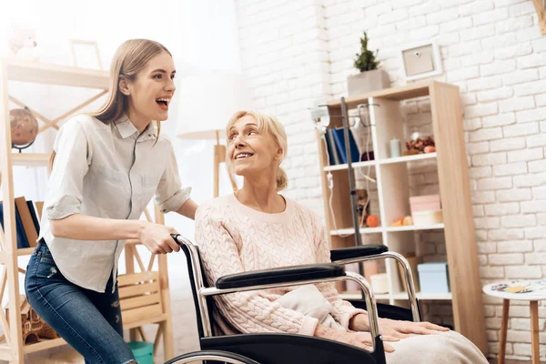 Girl nursing elderly woman at home and riding her in wheelchair