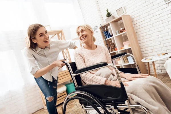 Girl nursing elderly woman at home and riding her in wheelchair