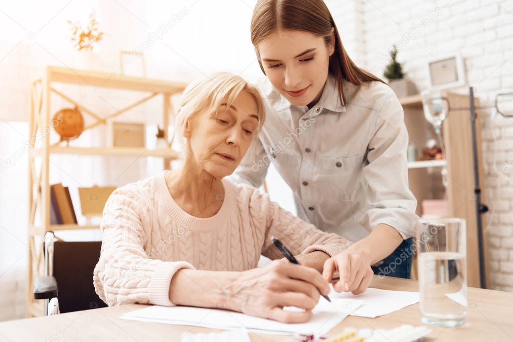 Girl nursing elderly woman in wheelchair and helping her writing
