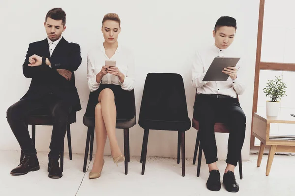 HR director woman in blouse and skirt sitting with coworkers and using smartphone