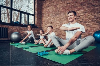 Baba, anne, kızı ve oğlu yeşil paspaslar üzerine oturan ve spor salonunda egzersiz yaparak 
