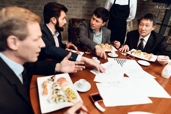 Men eating sushi on meeting with Chinese businessmen in restaurant