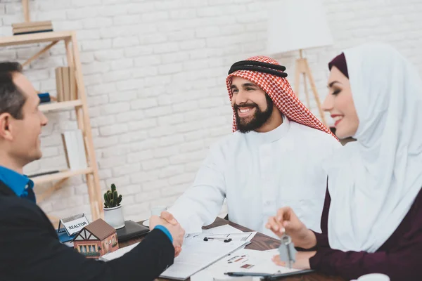 Realtor shaking hands with Arab man sitting in office