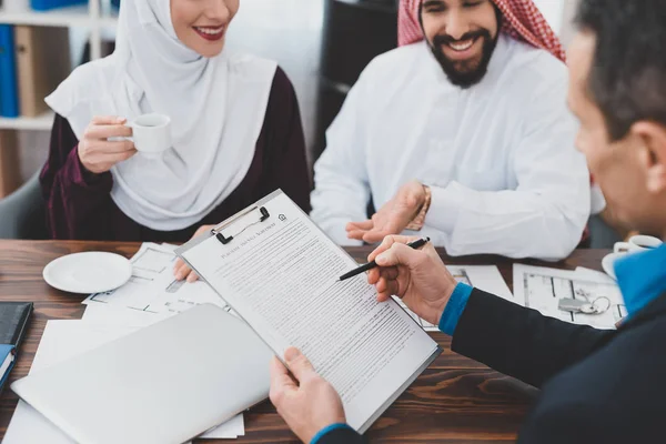 Realtor reading terms of purchase and sale agreement for young Muslim couple