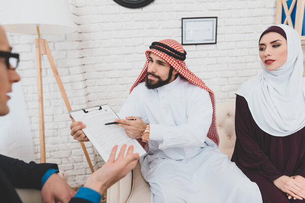 Arab in keffiyeh specifying terms of contract for purchase of house sitting next to woman in hijab