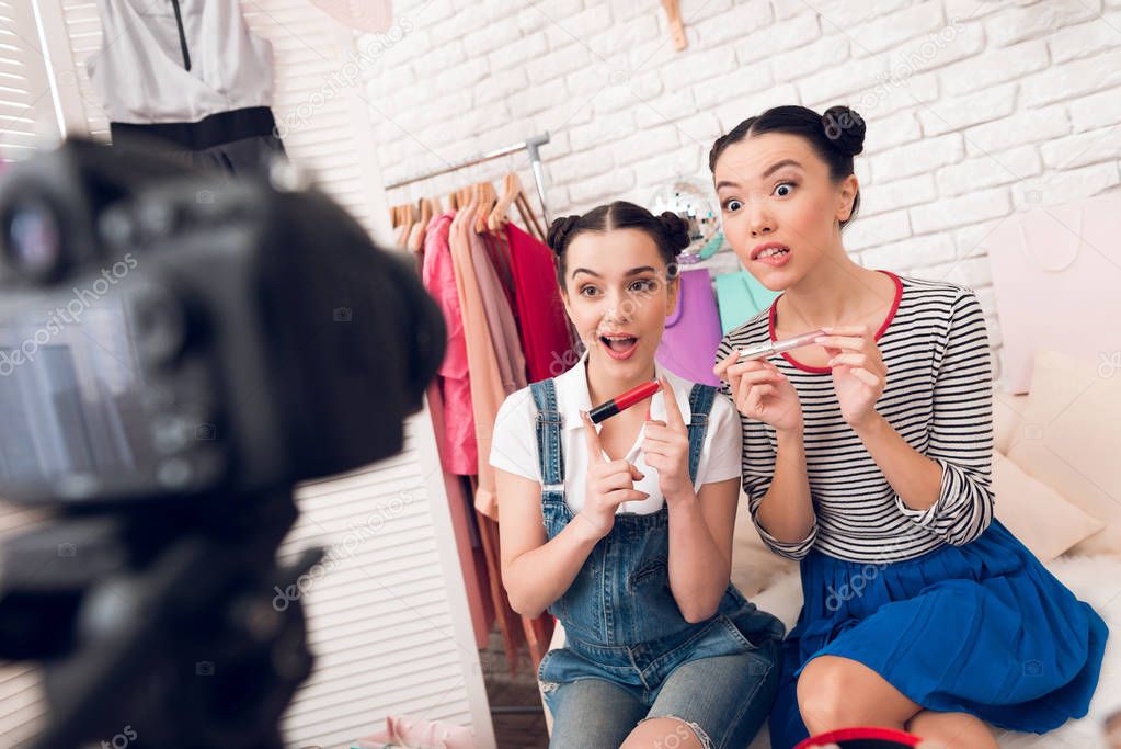 Two fashion blogger girls presenting colorful lipsticks to camera