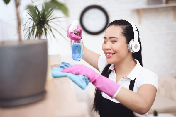 Asian maid in gloves wiping shelves and listening to music on headphones