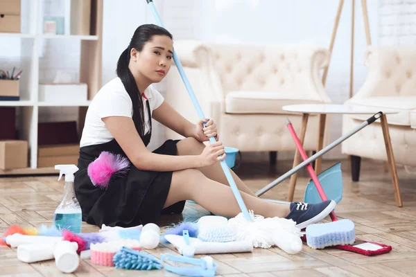 Upset Asian maid sitting on floor among cleaning accessories and tools