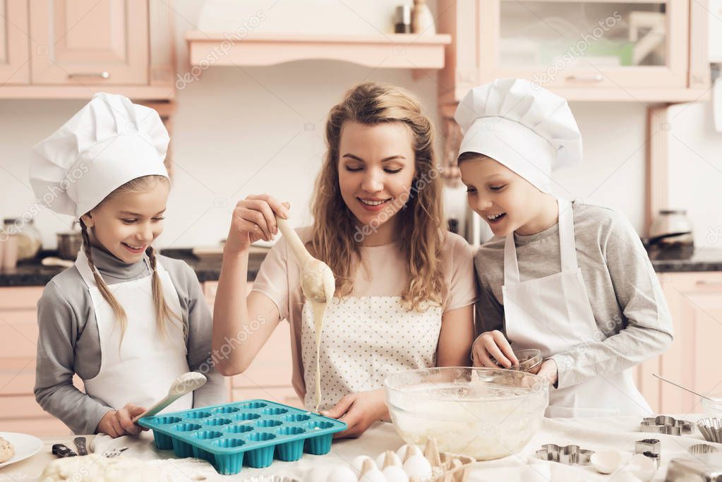 Mother teaching her children in white hats preparing cookies at kitchen