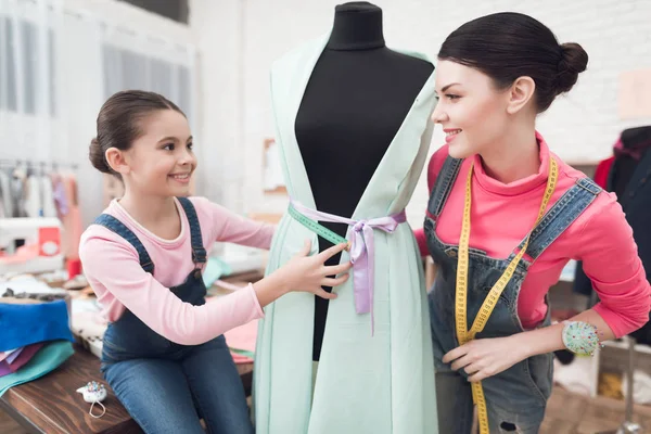 mother and daughter trying on clothes on mannequin while they working in sewing workshop