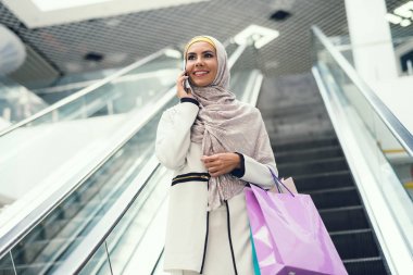 Alışveriş alışveriş torbaları ile yürüyüş ve smartphone üzerinde konuşurken Arap kadın