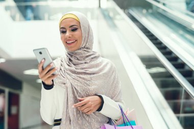 Alışveriş alışveriş torbaları ile yürüyüş ve smartphone kullanarak Arap kadın