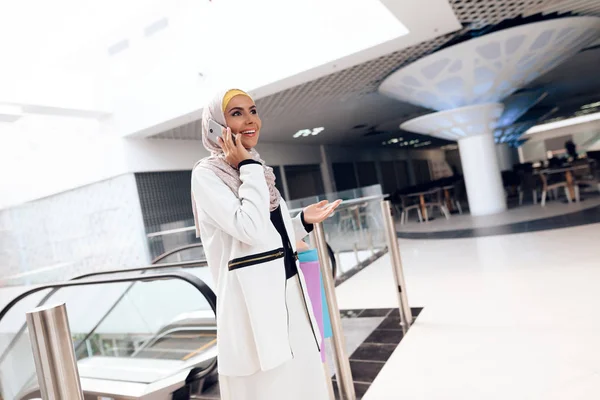 Arab woman walking in shopping mall with shopping bags and talking on smartphone