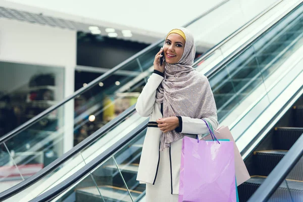 Arab woman walking in shopping mall with shopping bags and talking on smartphone