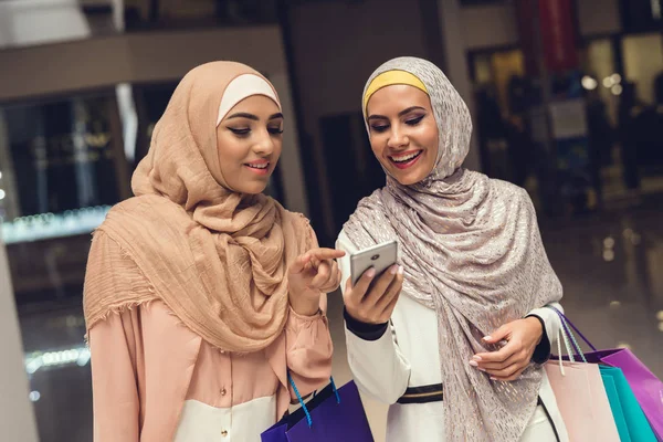 Arab women walking in shopping mall and using smartphone