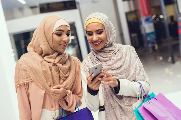 Arab women walking in shopping mall and using smartphone