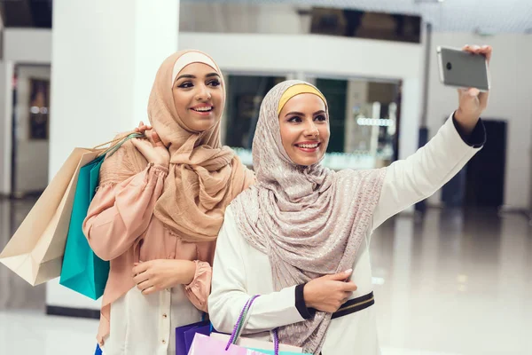 Arab women walking in shopping mall and taking selfie on smartphone